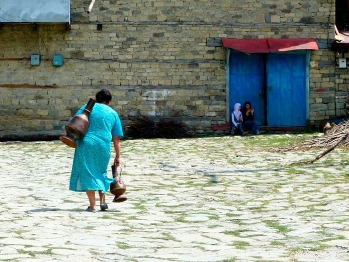 woman fetching water with hers copper vase in Lahic